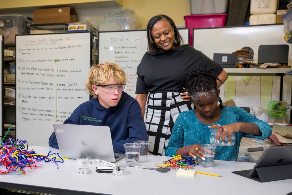 two students working on a STEM project with teacher overseeing the work being done.