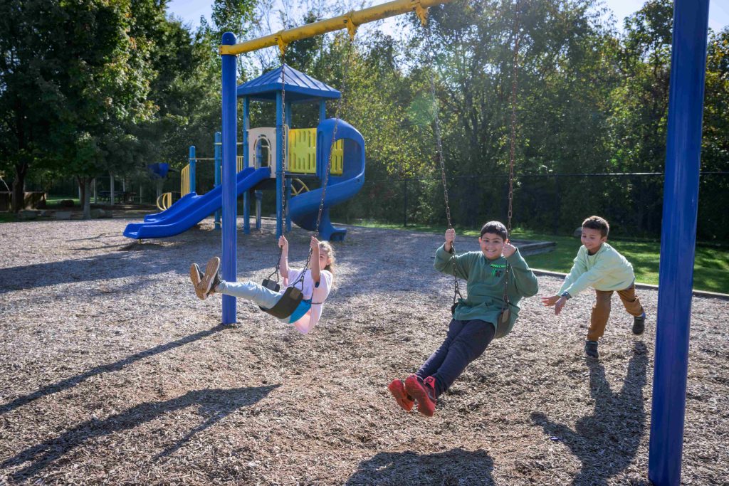 Three College School students on swings in the playground